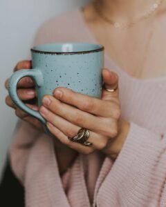 A close-up of a woman's hands holding a blue ceramic mug, wearing a cozy sweater.